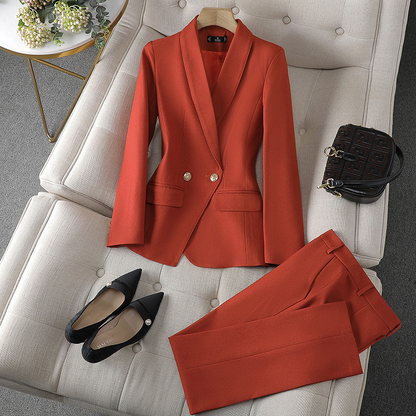 Ein gold-orangefarbener Blazer und eine passende Hose, ordentlich auf einer weichen Oberfläche angeordnet, kombiniert mit schwarzen spitzen Pumps und einer kleinen Handtasche.