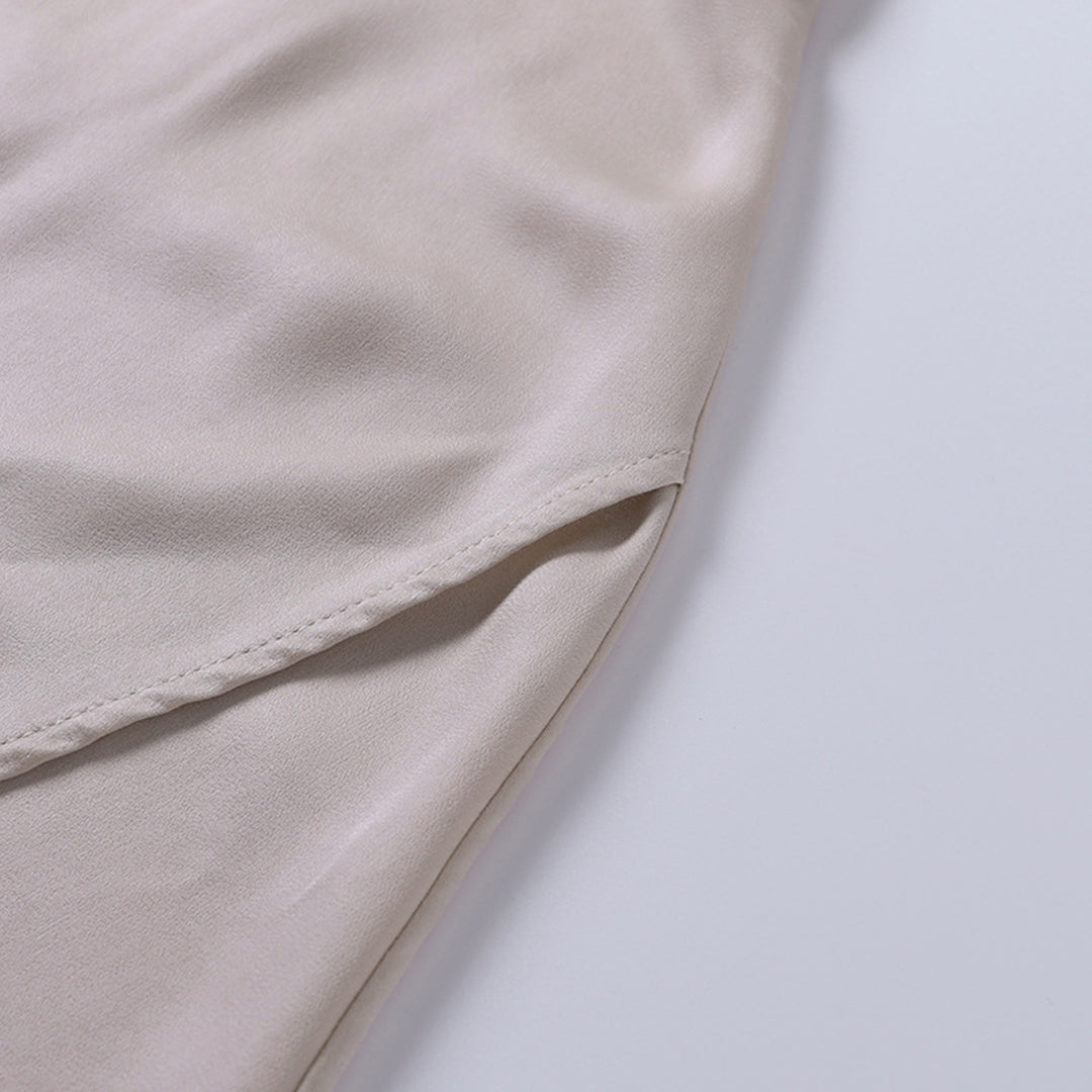 Eine Nahaufnahme des Seitenschlitzes eines beigen Kleides, die den Fall des Stoffes und die sauberen Nähte zeigt.